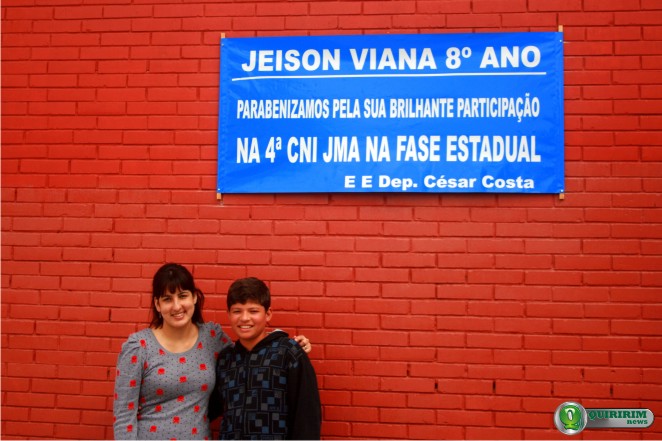 Professora Camile Giovanelli e Jeison Viana posam embaixo da faixa que parabeniza o aluno - Foto: Douglas Castilho/Quiririm News